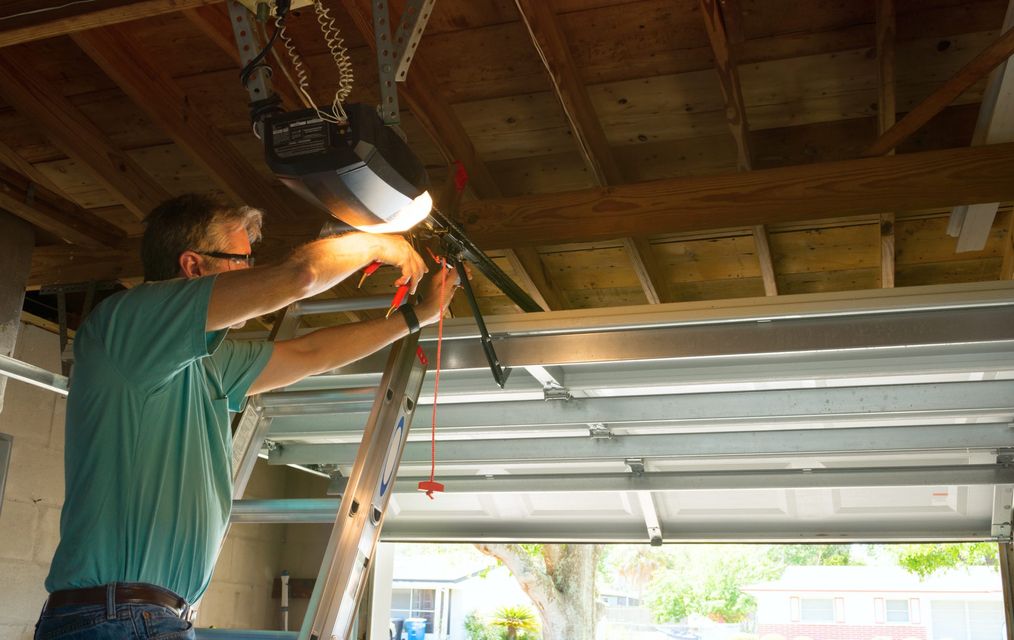 man standing on a ladder doing DIY garage door repairs