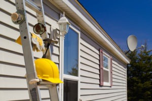 ladder leaning against home with yellow hardhat resting on step during home siding repair project