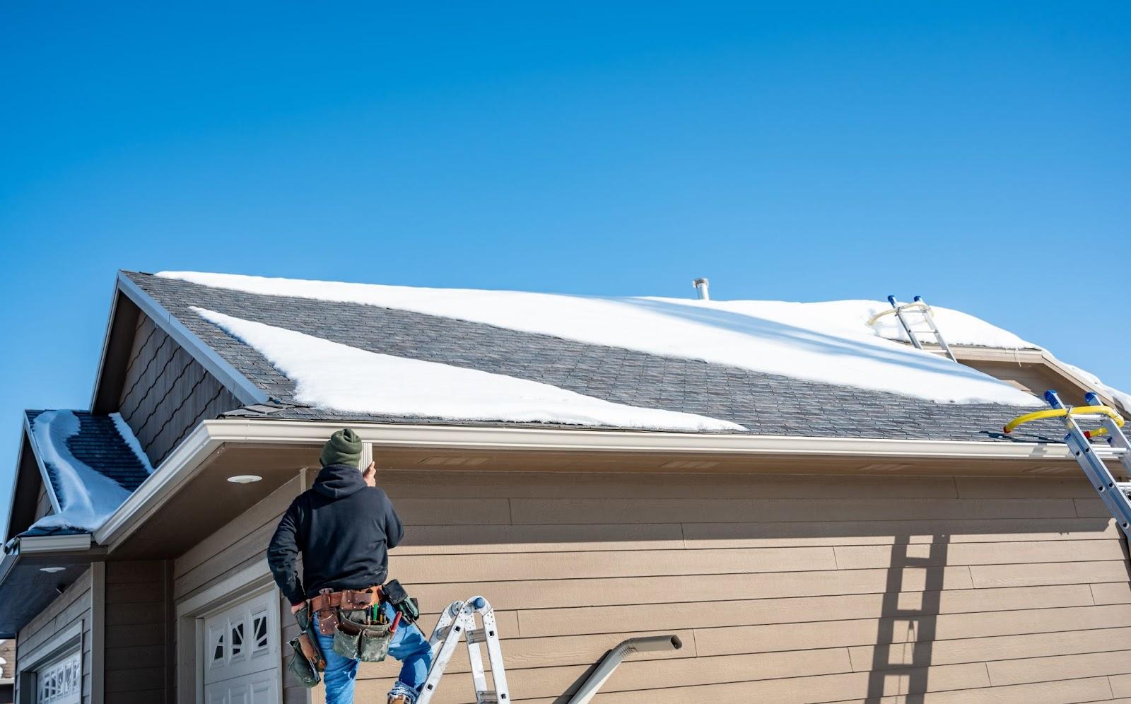 man installing new gutters on a home with snow on the roof