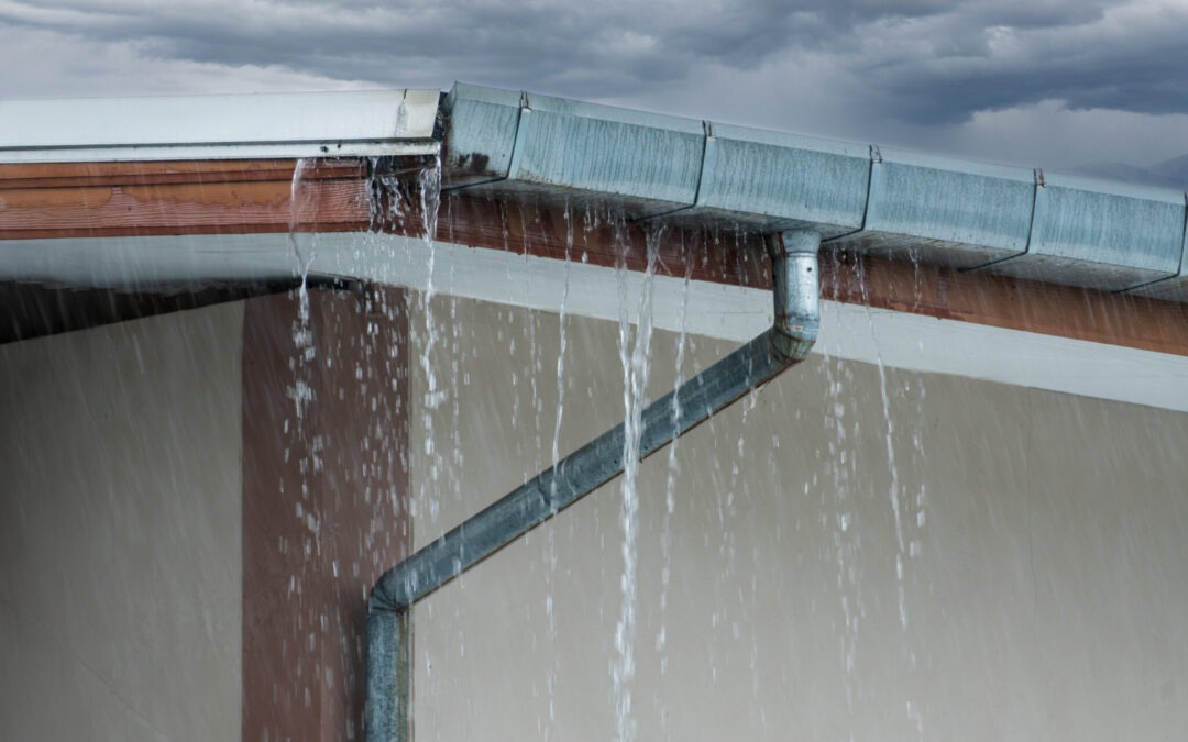 corner of a home. water is pouring from the gutter and downspout show the need to fix a gutter leak.