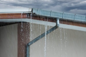 corner of a home. water is pouring from the gutter and downspout show the need to fix a gutter leak.