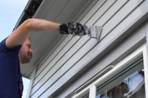 A man paints the exterior of a home to show can you paint vinyl siding